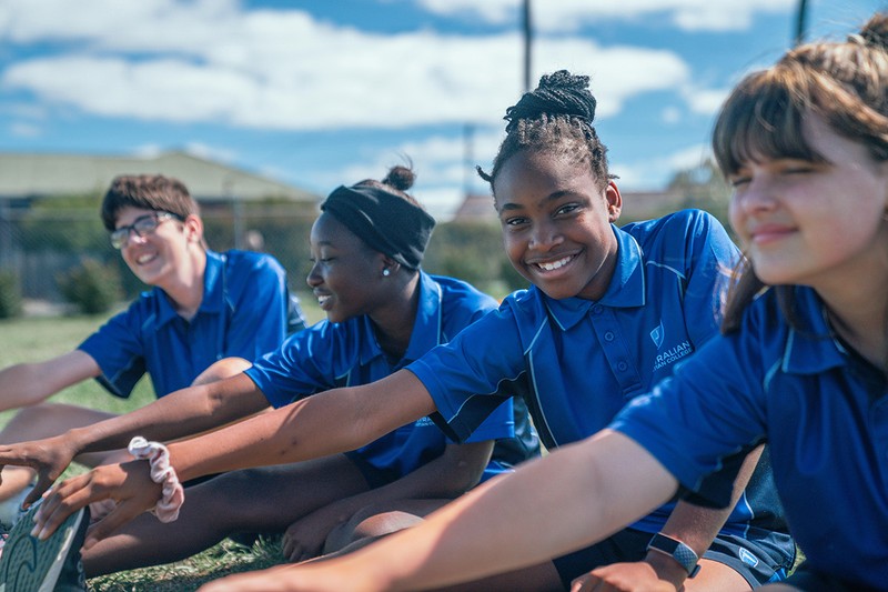 High school students in sports uniform stretching together on school oval