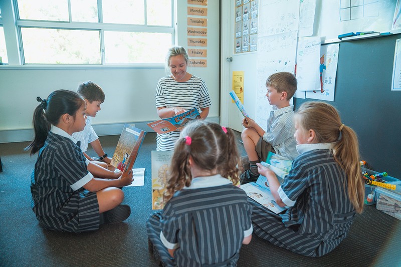 Group of kindergarten students sitting in circle with teacher while reading together