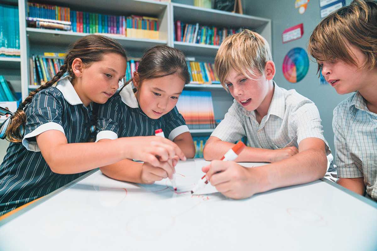 Primary aged students sitting around a table drawing together