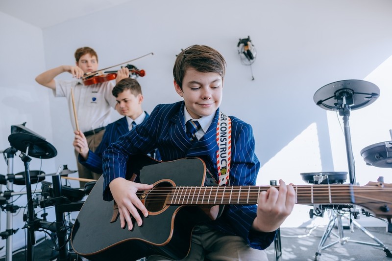 ACC Singleton student in blazer playing guitar