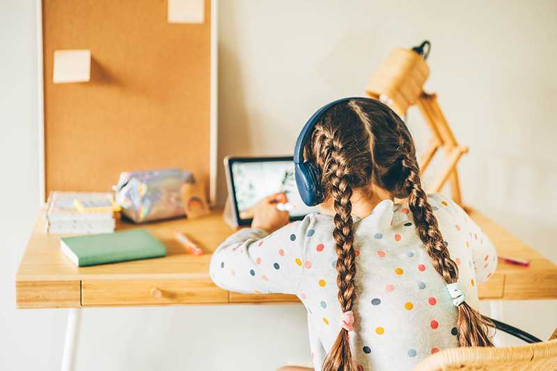 Girl with platted hair wearing headphones while completing schoolwork online from ipad