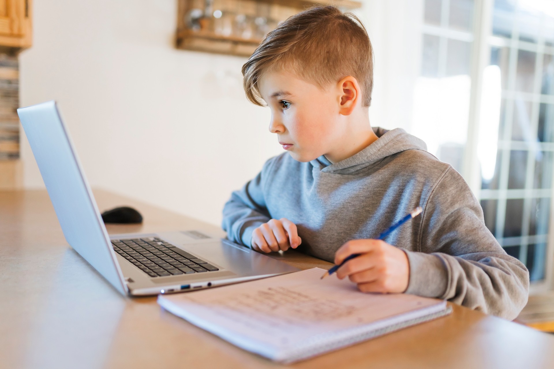 Primary school distance education student completing school work on laptop with notebook